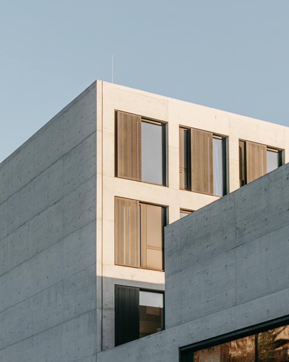 Concrete office building with recessed wooden windows under a clear sky